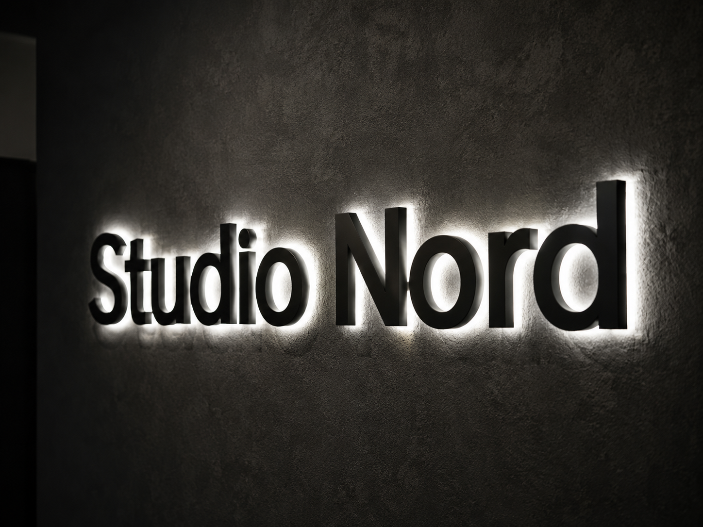 Schwarze, dreidimensionale Leuchtschrift „Studio Nord“ mit hellem Rücklicht an einer dunklen Wand.