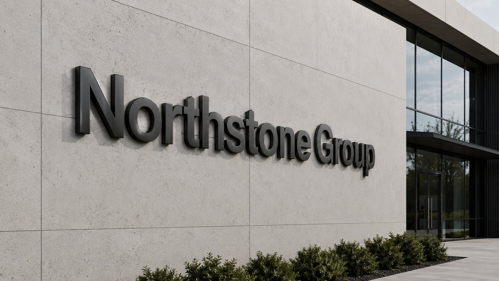 Schwarze 3D-Buchstaben "Northstone Group" an heller Betonfassade neben großen Glasfenstern, niedrige Büsche am Gebäudefuß.