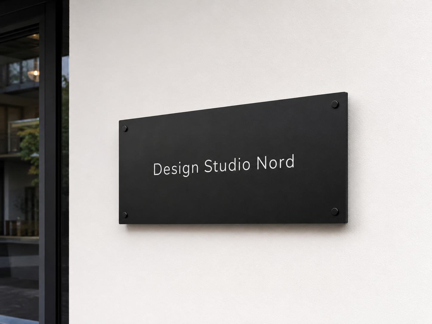 Schwarzes Wand­schild mit weißer Schrift "Design Studio Nord" an einer hellen Fassade neben einem Fenster.