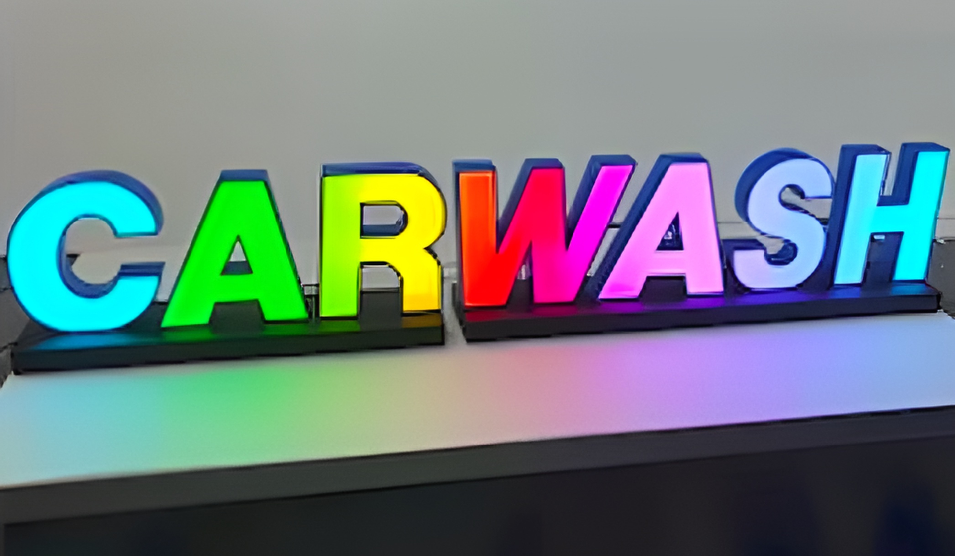 Bunte 3D-Buchstaben mit dem Wort CARWASH auf schwarzer Basis, beleuchtet wie ein Leuchtschild