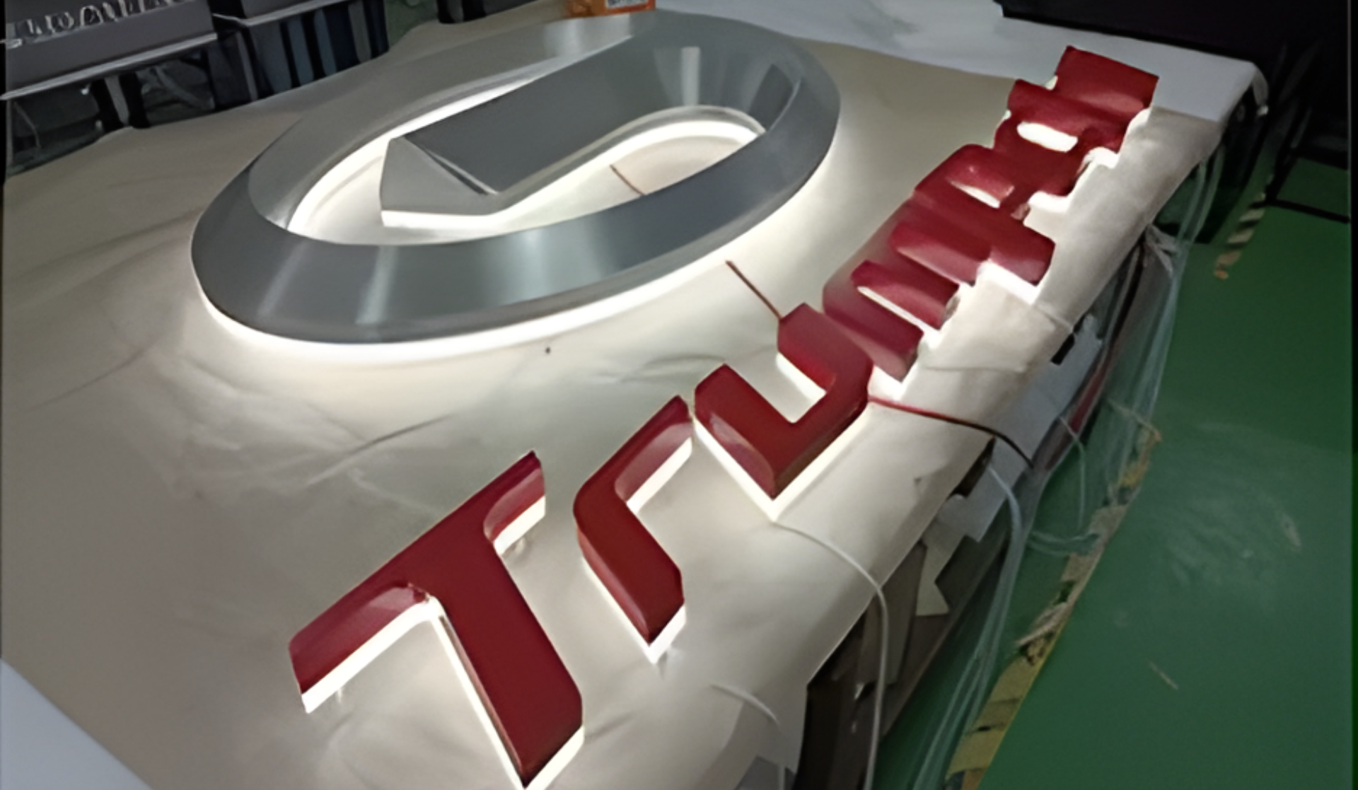 Beleuchtetes Tesla-Logo und rote 3D-Buchstaben auf einem weißen, teilweise abgedeckten Schild
