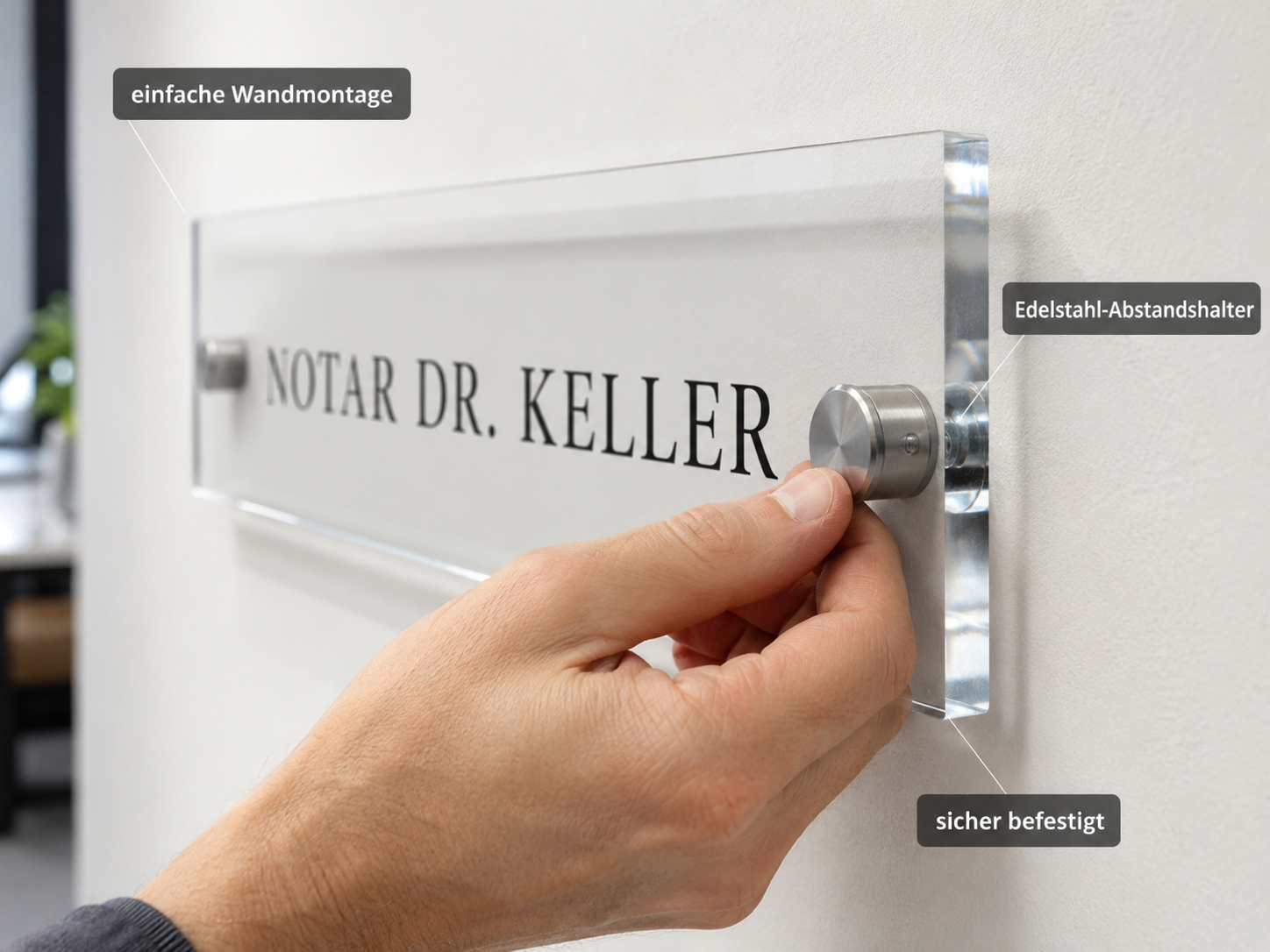 Hand befestigt ein transparentes Namensschild mit Edelstahl-Abstandshaltern an einer Wand; „NOTAR DR. KELLER“ sichtbar
