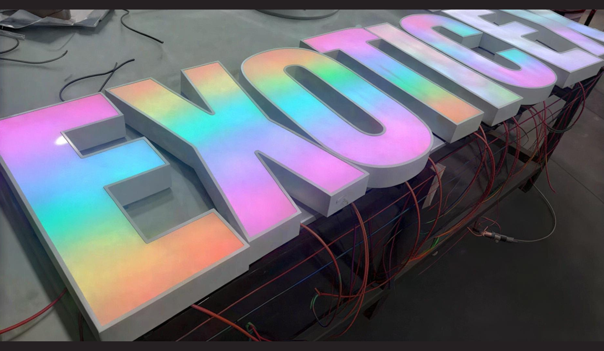 Große leuchtende 3D-Buchstaben mit Regenbogenverlauf, teilweise verkabelt auf einer Arbeitsfläche