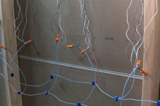 Mehrere lose elektrischen Leitungen mit orangefarbenen und blauen Drahtverbindern hängen in einer Wandöffnung zwischen Holzständern.