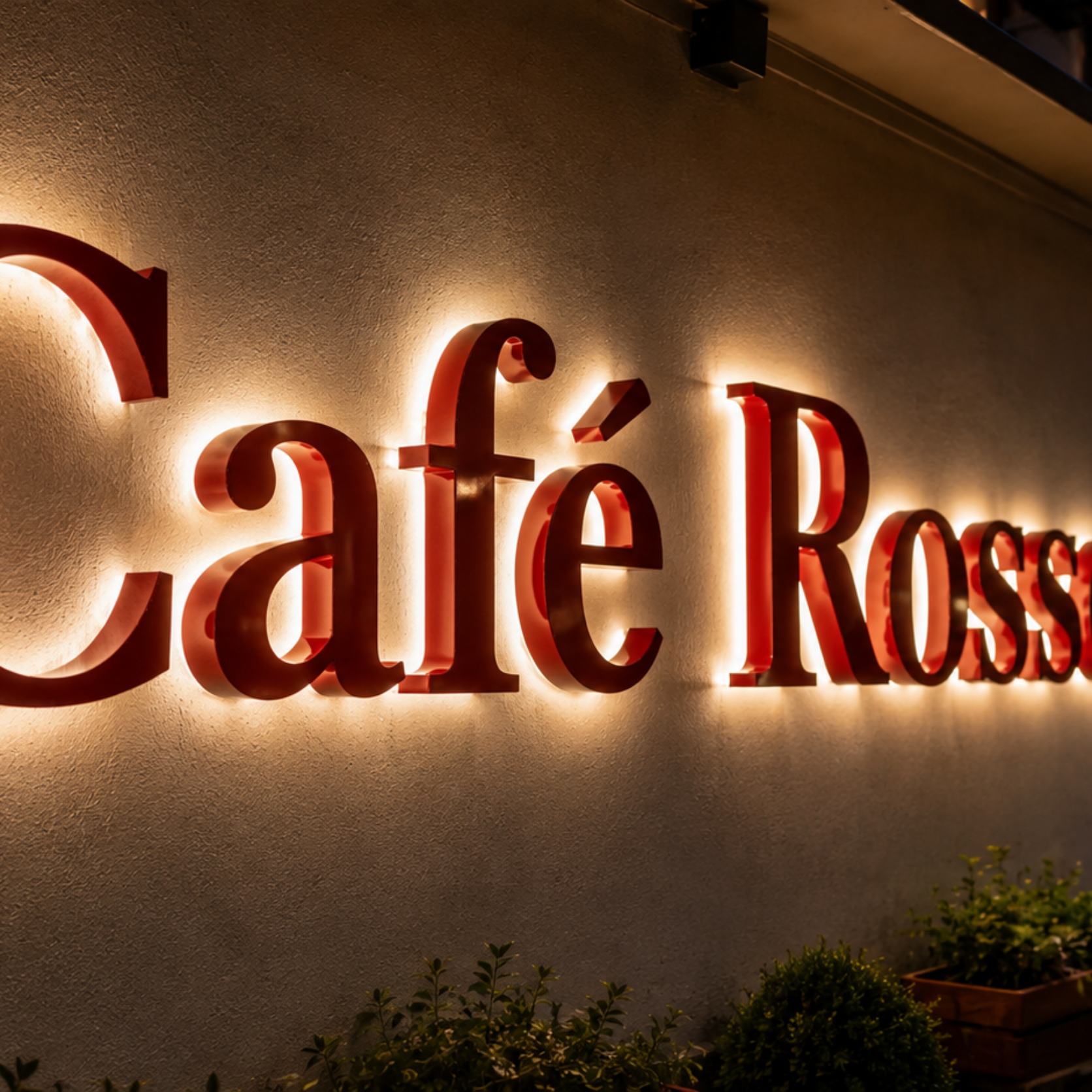 Leuchtendes rotes Schild mit der Aufschrift „Café Rosso“ an der Fassade eines Cafés bei Abendlicht.