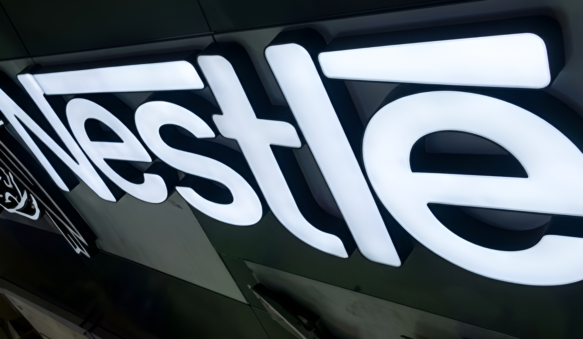 Leuchtende weiße Buchstaben eines schräg aufgenommenen Tesla-Schilds an dunkler Wand