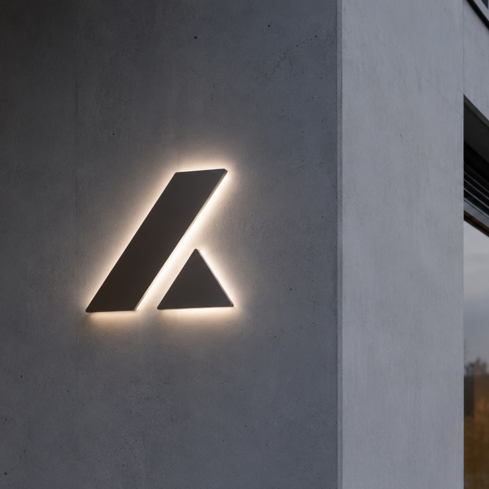 Schwarzes, beleuchtetes Firmenlogo aus zwei geometrischen Formen (schräges Rechteck und Dreieck) an einer grauen Betonfassade bei Dämmerung