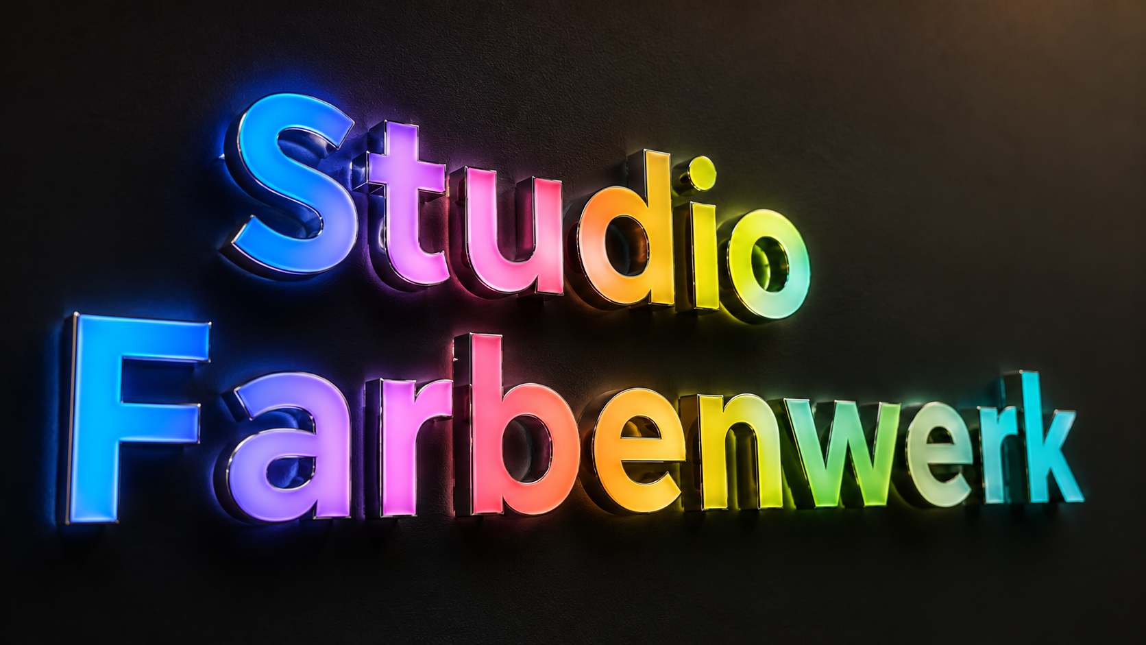 Leuchtende, mehrfarbige 3D-Buchstaben an schwarzer Wand mit dem Text "Studio Farbenwerk" in blau, pink, gelb und grün.