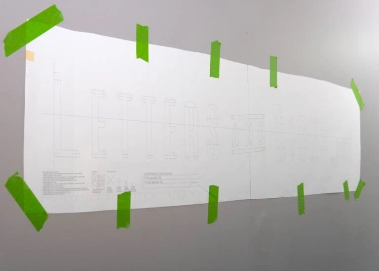 Langes weißes Papier mit feiner Bleistiftzeichnung, an einer Wand mit grünem Malerkrepp in mehreren Stellen befestigt.